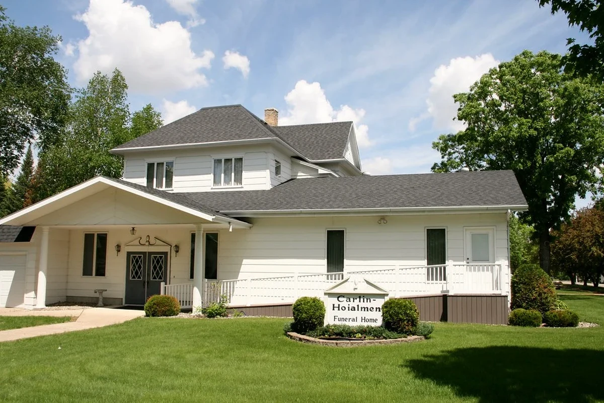 Exterior-style funeral home scene with a calm entrance and memorial flowers in a small town